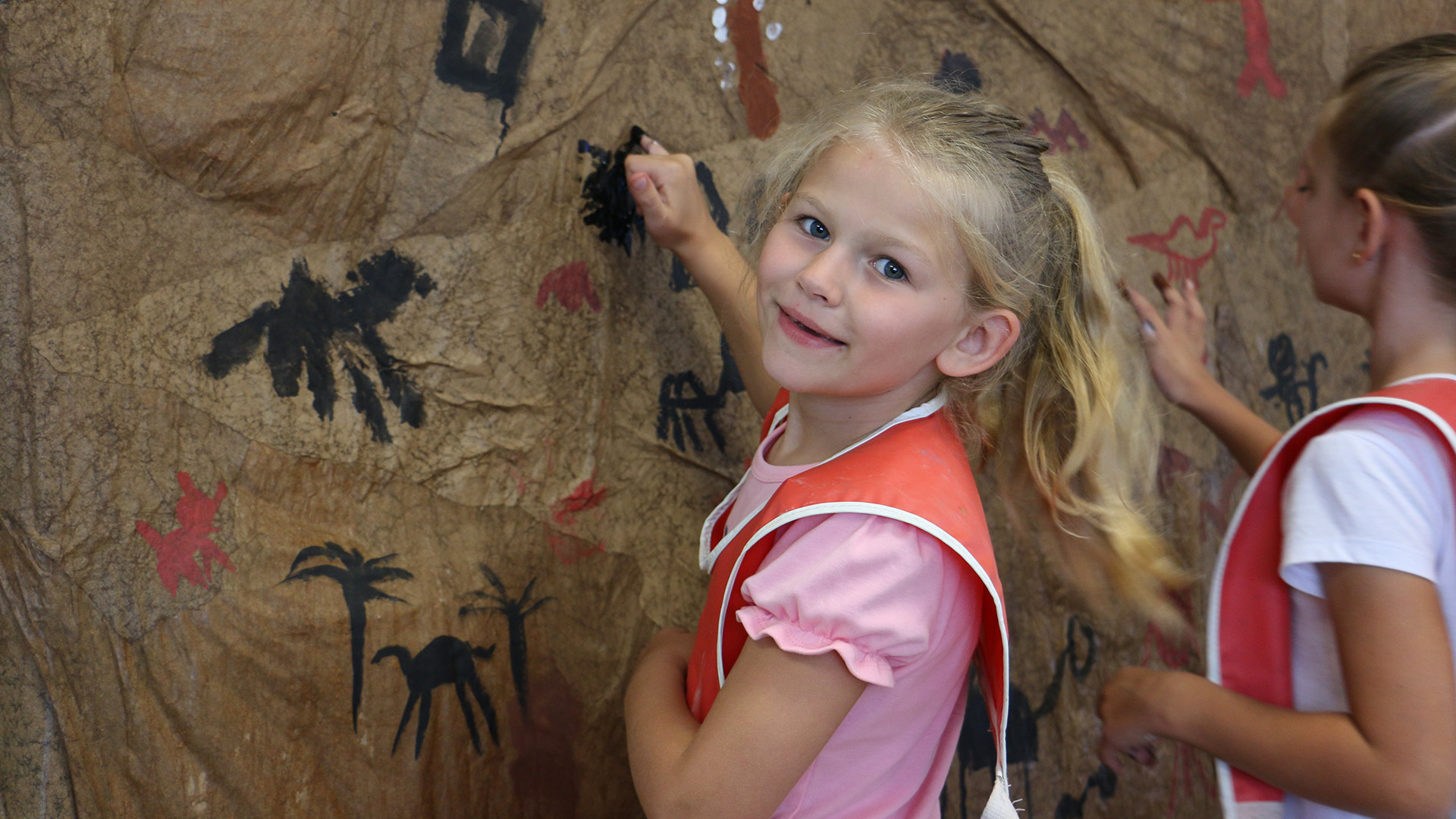 A girl painting on a large piece of paper on a wall.